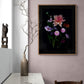 A framed dark botanical print of colourful Dahlias, Cosmos, Asters and Mallow on a black background, hung on a pale pink wall.