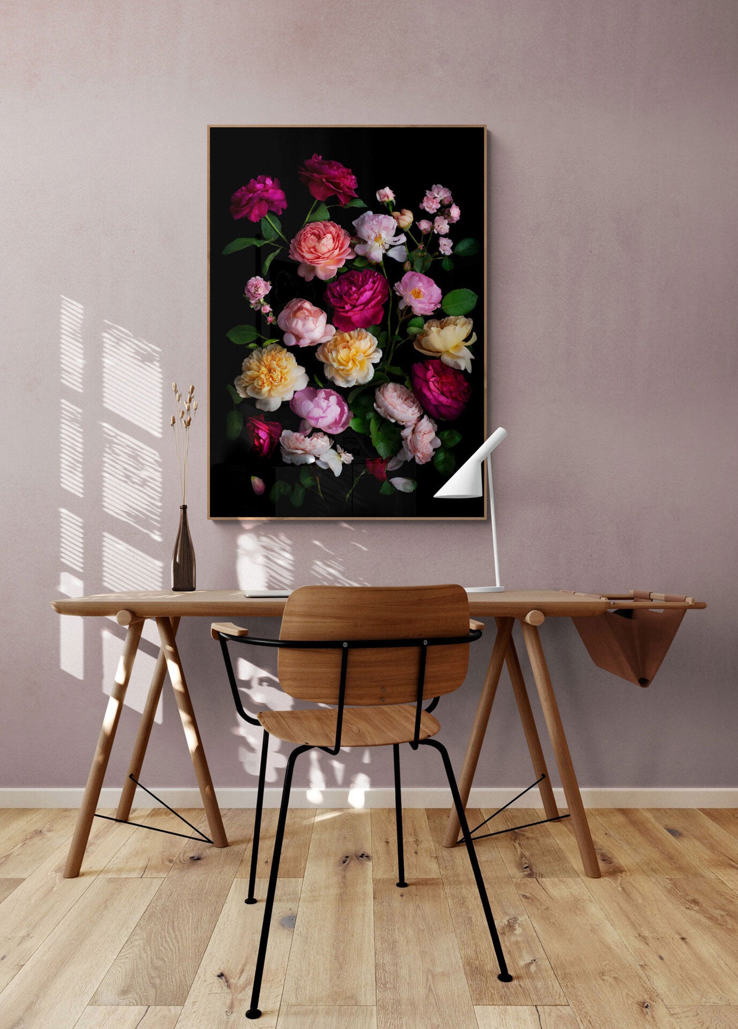Framed dark botanical print of different coloured roses photographed on a black background hung on a pale pink coloured wall.
