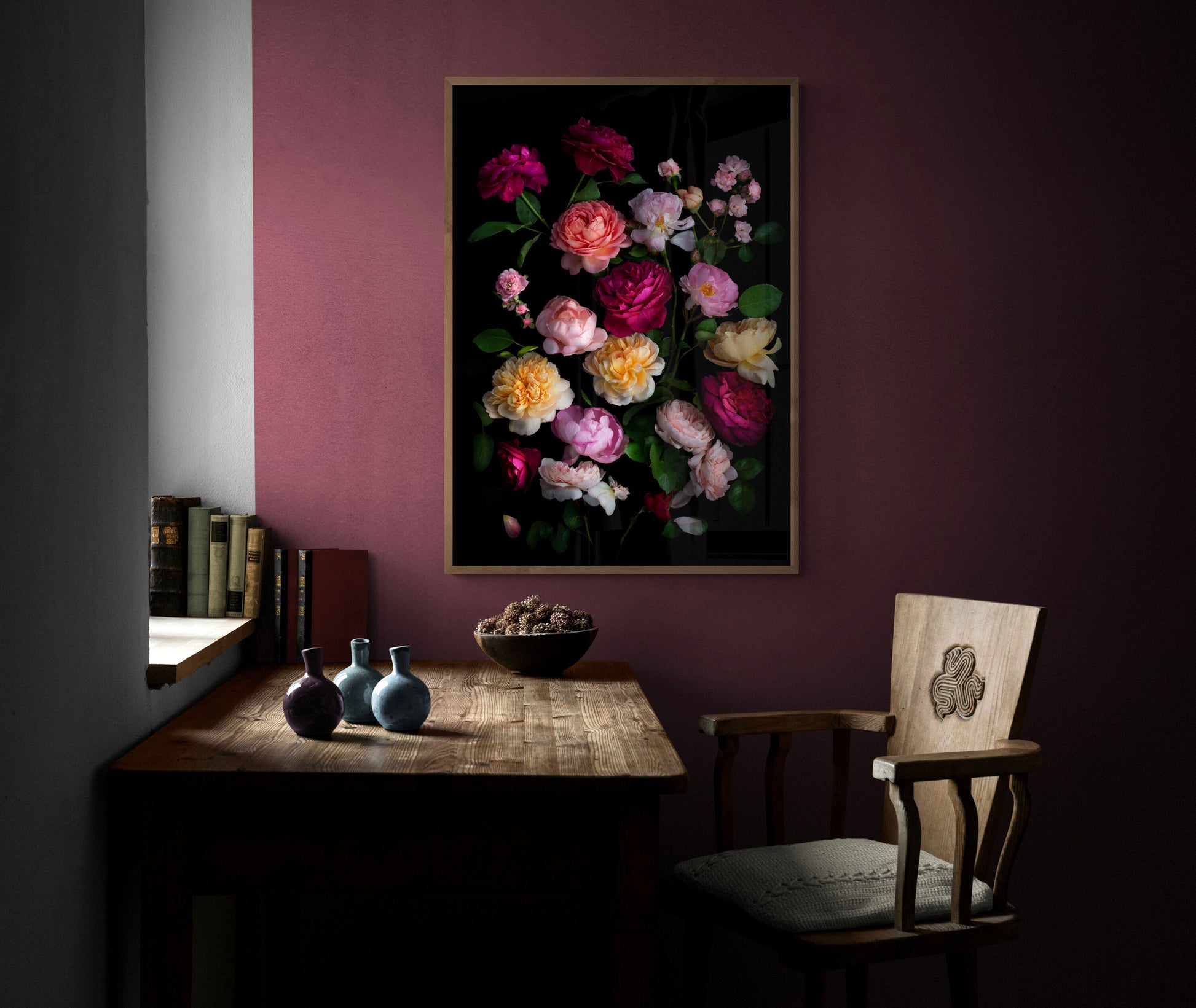 Framed dark botanical print of different coloured roses photographed on a black background hung on a plum coloured wall.