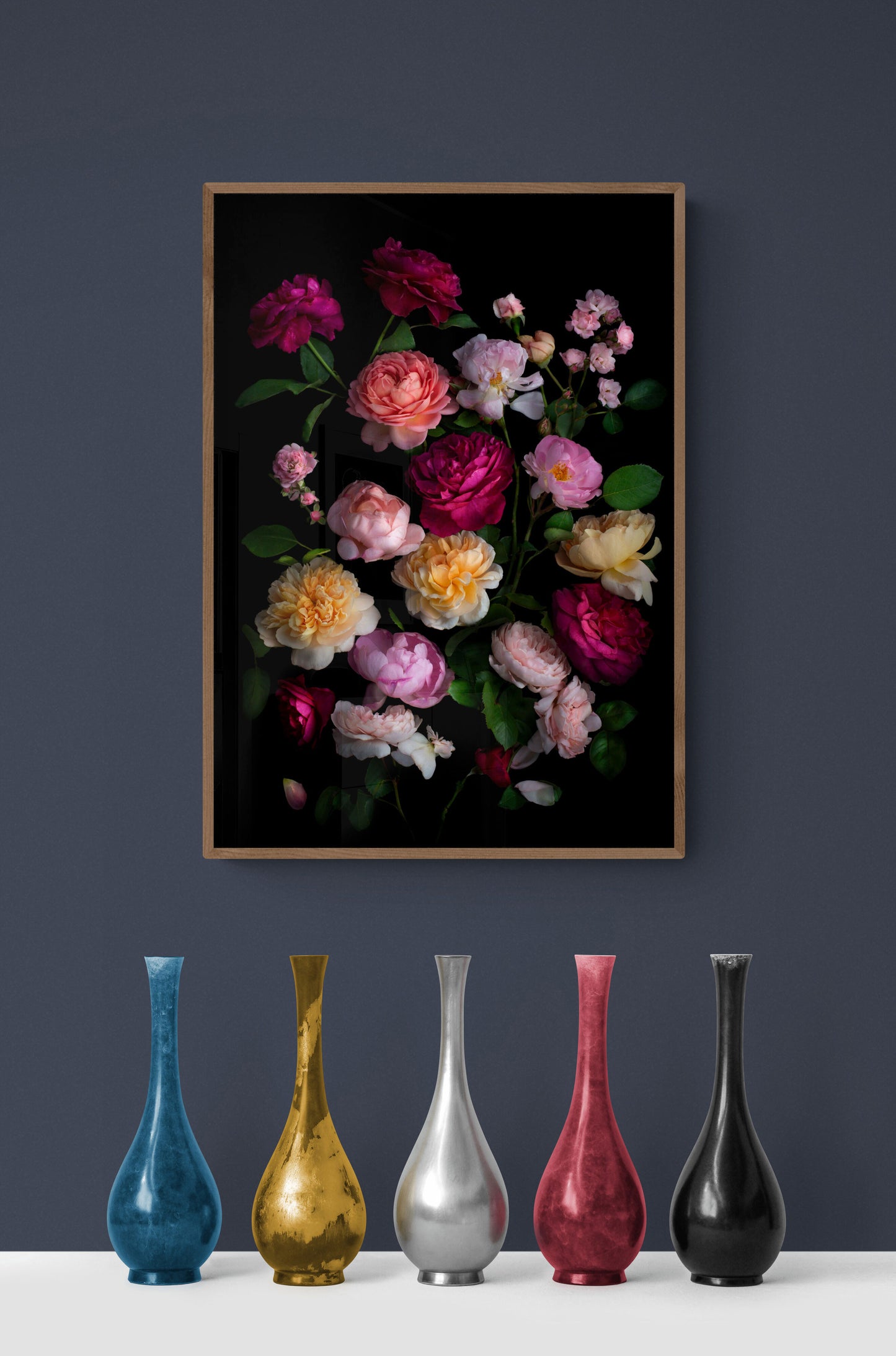 Framed dark botanical print of different coloured roses photographed on a black background hung on a gray coloured wall.