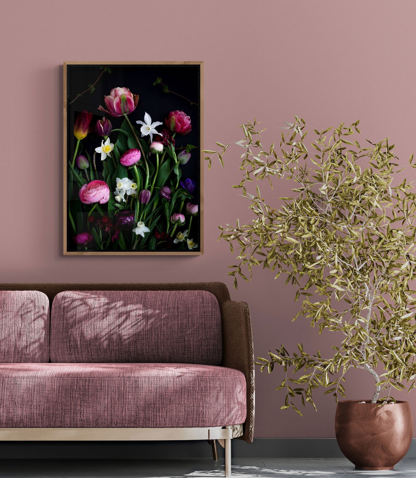 Portait format dark botanical print of Spring flowers photographed on a black background hung above a sofa on a pale warm pink wall.